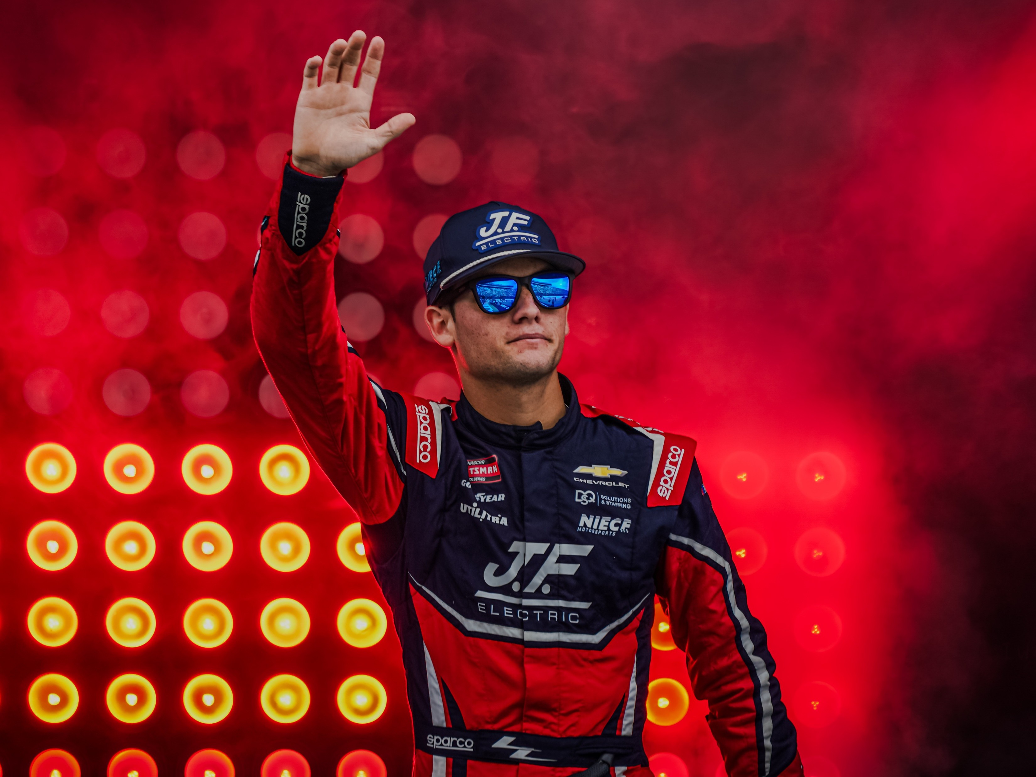 NASCAR driver waving during introductions against a vivid red background